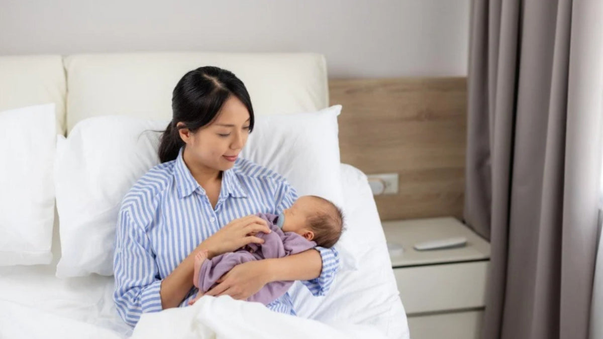 New mother resting with newborn during confinement in a Singapore home with confinement essentials nearby