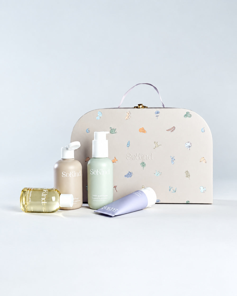 Four SoKind Dear Baby skincare products displayed in front of a patterned carry case