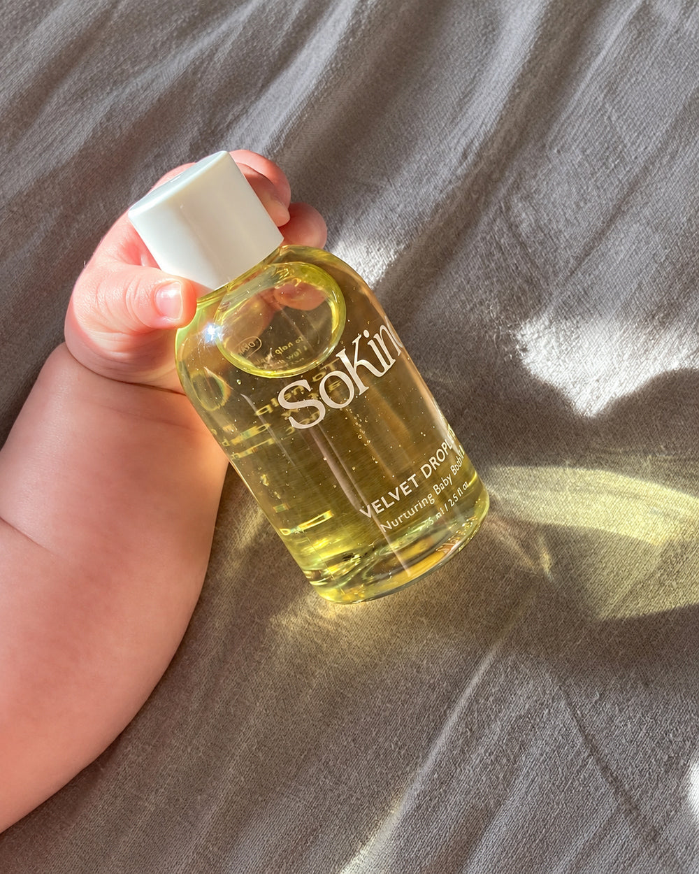 Baby holding a bottle of SoKind Velvet Drops Nurturing Baby Body Oil